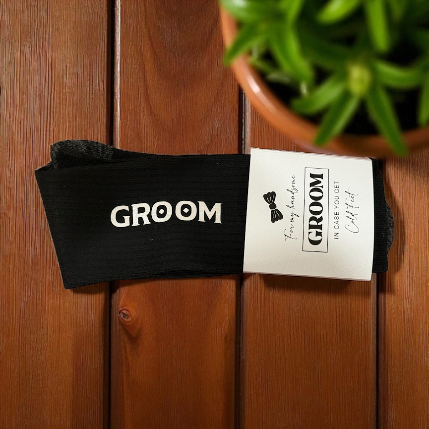 Black 'GROOM' pouch with a card on a wooden surface with a plant in the background