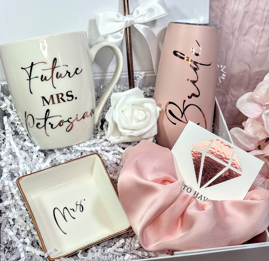 White and Blush Future Mrs. engagement gift box featuring a personalized white ceramic mug with gold lettering, a chic porcelain ring dish, a stainless steel champagne flute, a satin hair scrunchie, and bridal shower must-haves, all styled in a luxury white keepsake box with satin bow — the perfect personalized bride-to-be gift for engagements, weddings, or bridal showers.