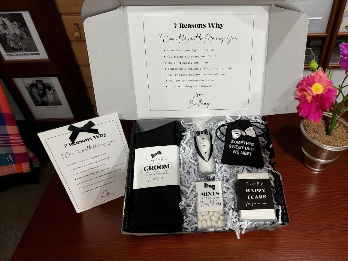 Gift box with wedding-themed items including a tuxedo, bow ties, and a card on a wooden surface.