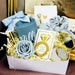 A variation of NIMA Gifts Bridesmaid proposal gift box in Dusty Blue and Gold Wedding Color. The gift box includes a dusty blue tumbler, straw with a dusty blue bow, a gold diamond pen, gold foiled lip balm, "I Can't Say I Do Without You" Gold hair tie on a gold foiled diamond card, personalized gold mirror, dusty blue bow tie hair scrunchy and a foam rose to match gift box colors Personalized Mirror is not included in this variation.