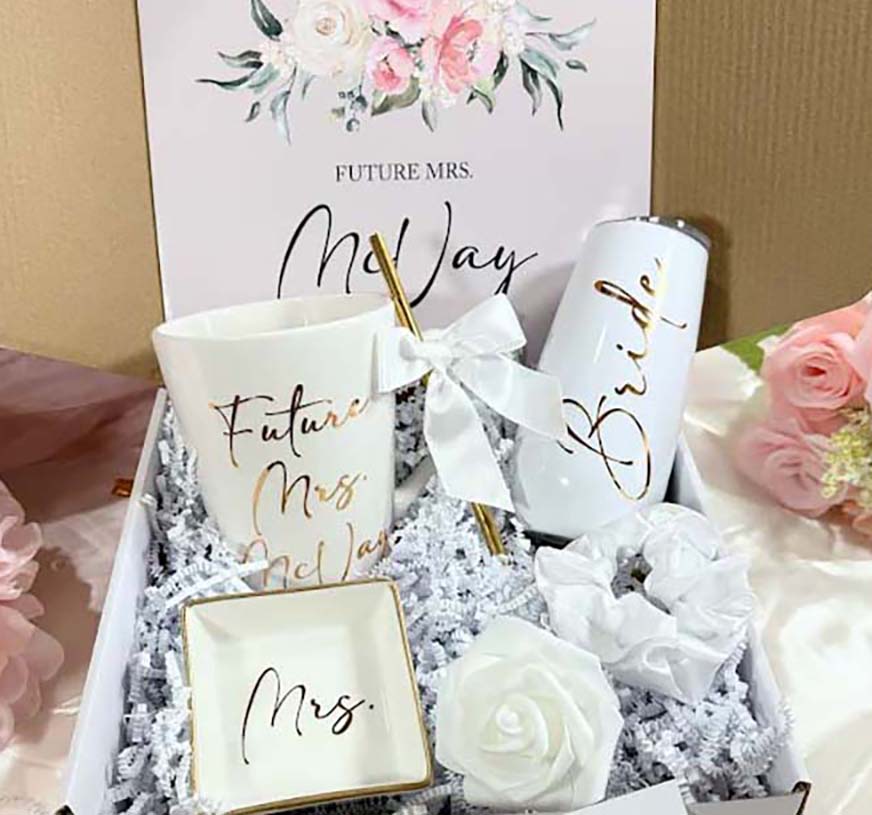 Gift set for a future bride with 'Future Mrs.' and 'Bride' mugs, a ring box, and flowers.