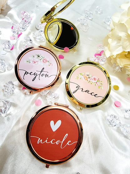 Bridesmaid, jr. bridesmaid, or flower girl Compact mirror personalized with a girls name and with a heart design, placed on a white packaging box with a gold heart, surrounded by flowers. A great thank you gift or a birthday gift for a younger teenager.