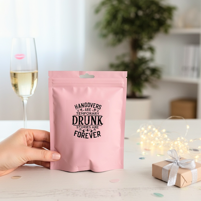 Pink pouch with humorous text held by a hand, with a glass of wine and decorative lights in the background.