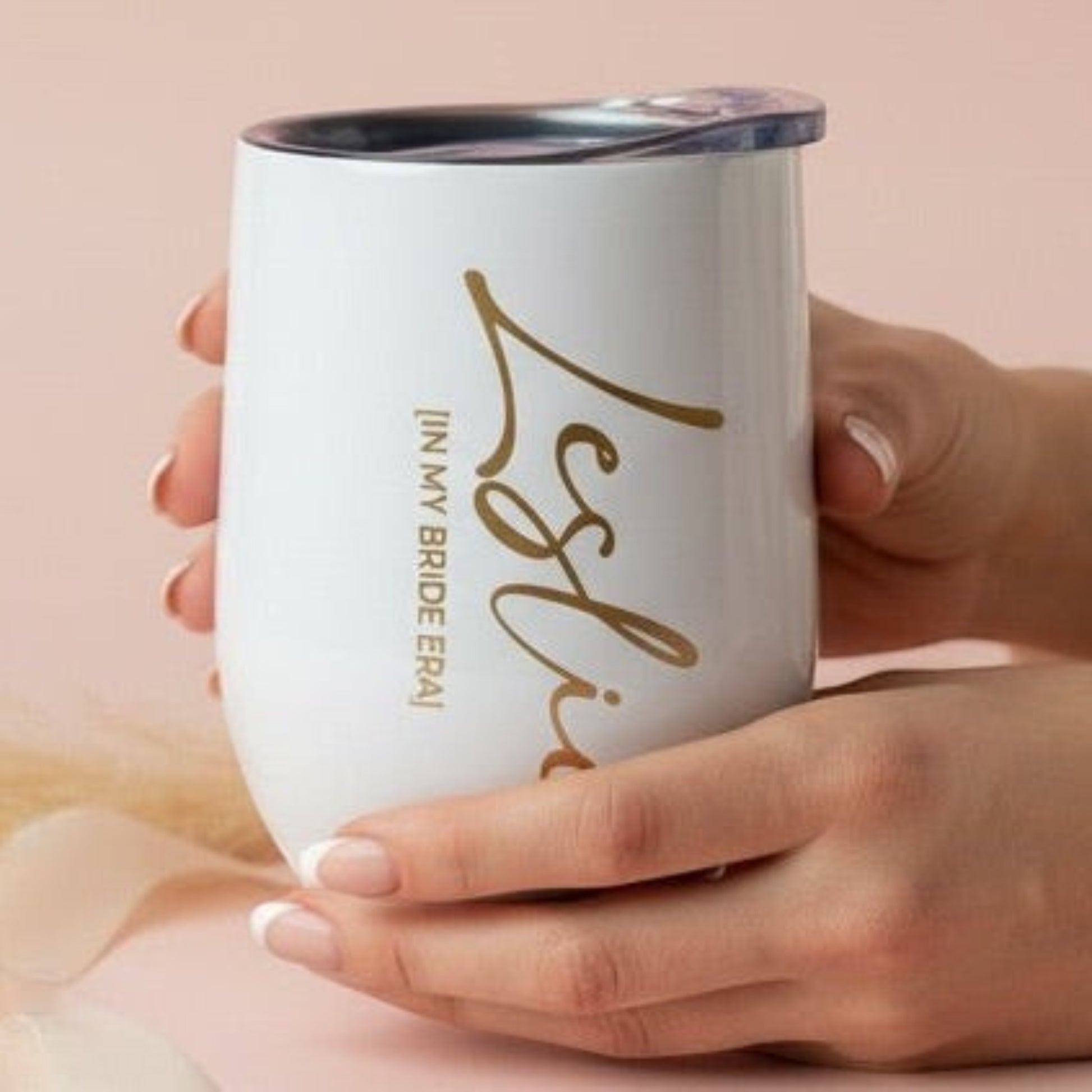 Person holding an engraved and personalized bride to be white stainless steel wine tumbler with gold text on a pink background