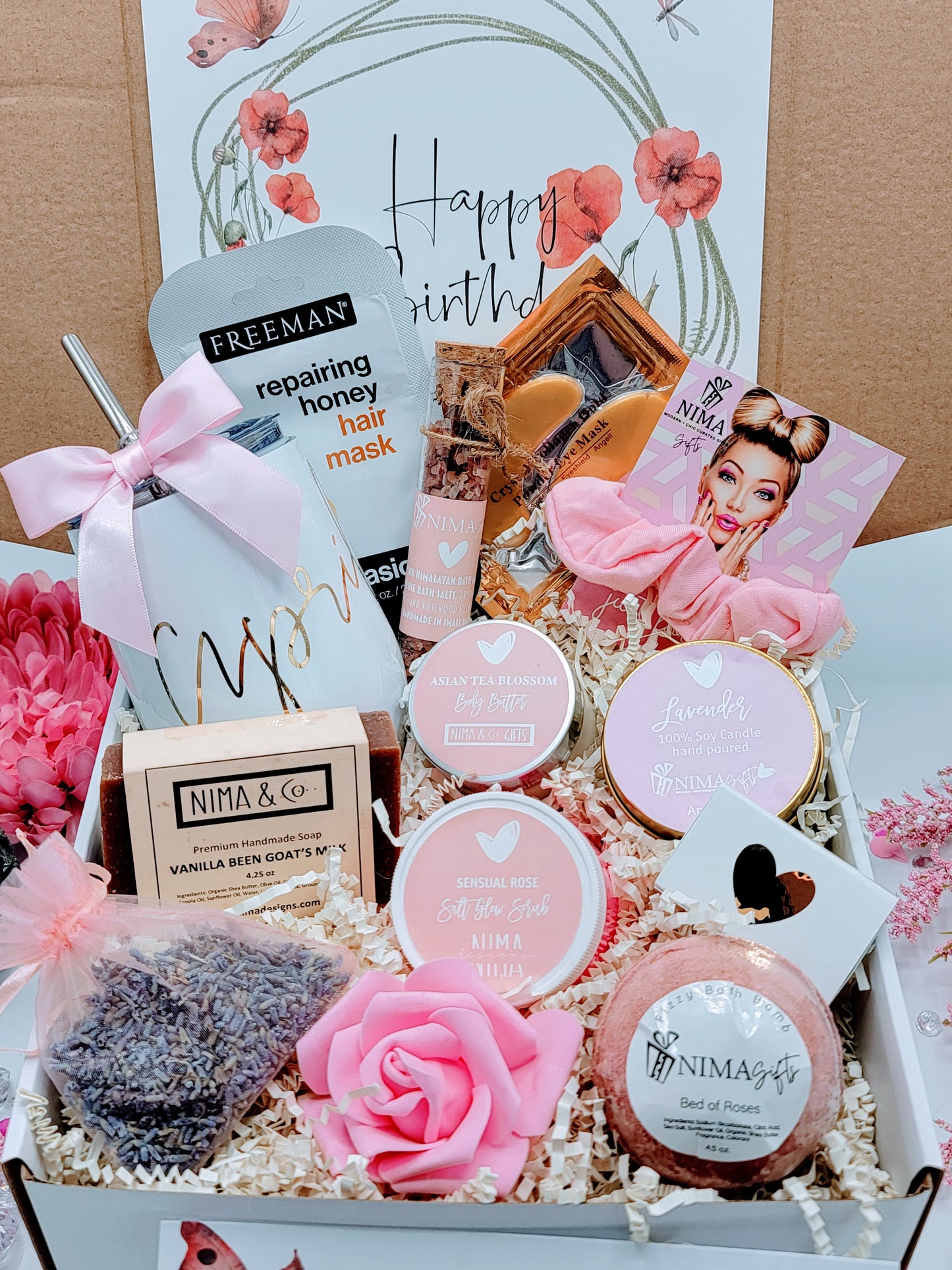 Open view of personalized spa gift box showing a white wine tumbler, metal straw with satin bow, lavender soy candle with dried flowers, glass bath crystal tube, printed greeting card, foam rose, and shredded paper inside a custom-design box.