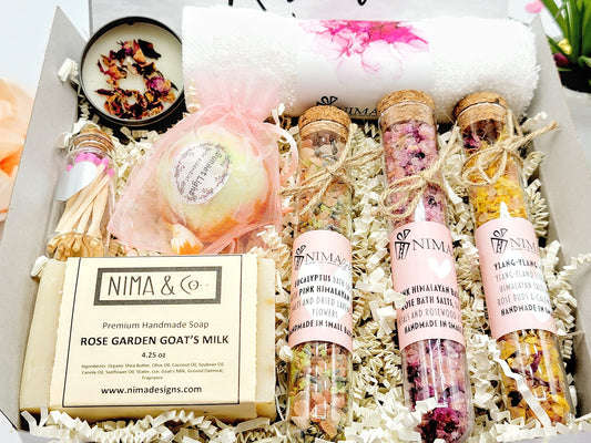 A gift box filled with bath and body products. The gift contains a white wash towel, a small bath bomb, three glass tubes filled with bath salts, and a Premium Handmade Soap, and a small candle with matches to finish the gift box.