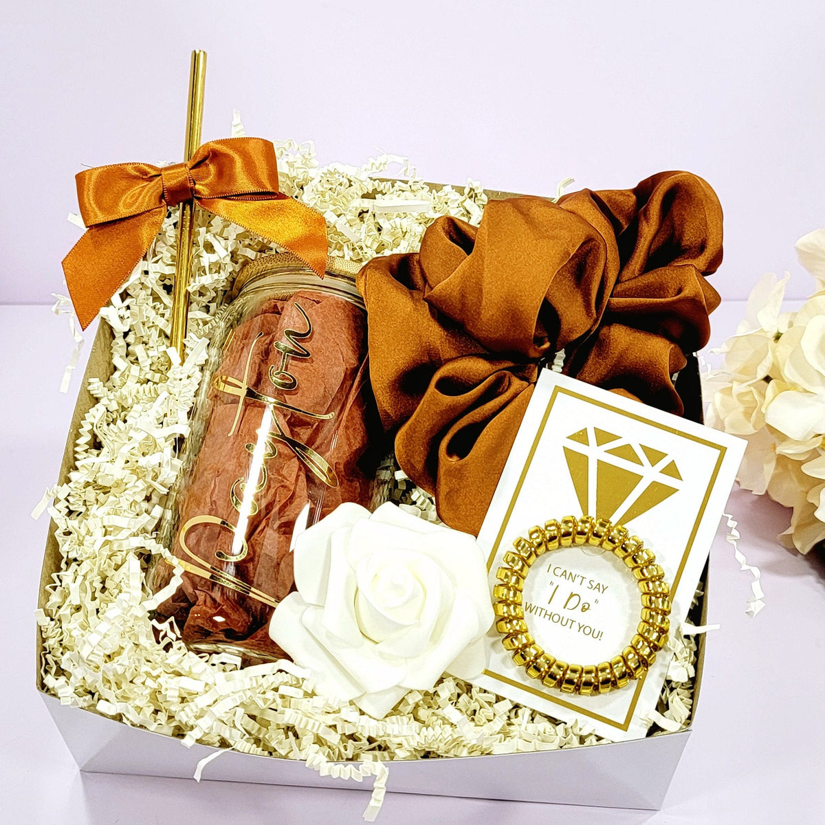 A bridesmaid proposal gift box that contains a 16oz glass tumbler with gold lettered name, gold straw with matching satin bow, a satin burnt orange hair scrunchie, a gold telephone wire scrunchie by NIMA Gifys