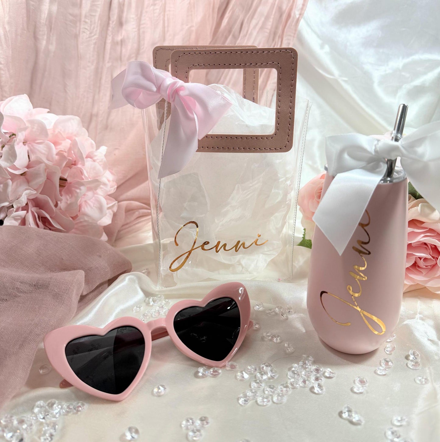 Personalized Clear Tote Bag Gift Set with Leatherette handles in dusty rose and a white bow.Set includes a 6oz blush campaigned tumbler personalized with the bridesmaid name, a pair of blush colored heart shaped sunglasses and a blush silk scrunchie (nto shown).
