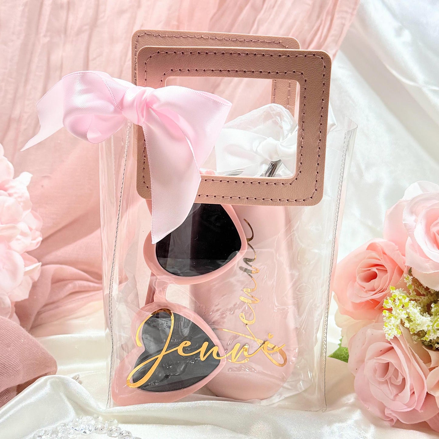 Personalized Clear Tote Bag Gift Set with Leatherette handles in dusty rose and a white bow.Set includes a 6oz blush campaigned tumbler personalized with the bridesmaid name, a pair of blush colored heart shaped sunglasses and a blush silk scrunchie (nto shown).