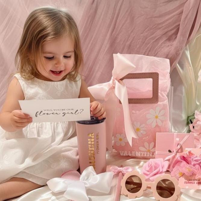 Flower Girl Proposal Gift Bag with PU leather handles, filled with personalized keepsakes like tumbler, scrunchie, sunglasses, and greeting card. A playful alternative to the flower girl proposal box, this personalized flower girl gift makes the perfect junior bridesmaid proposal gift, bridal party wedding gift, or kids wedding gift keepsake.