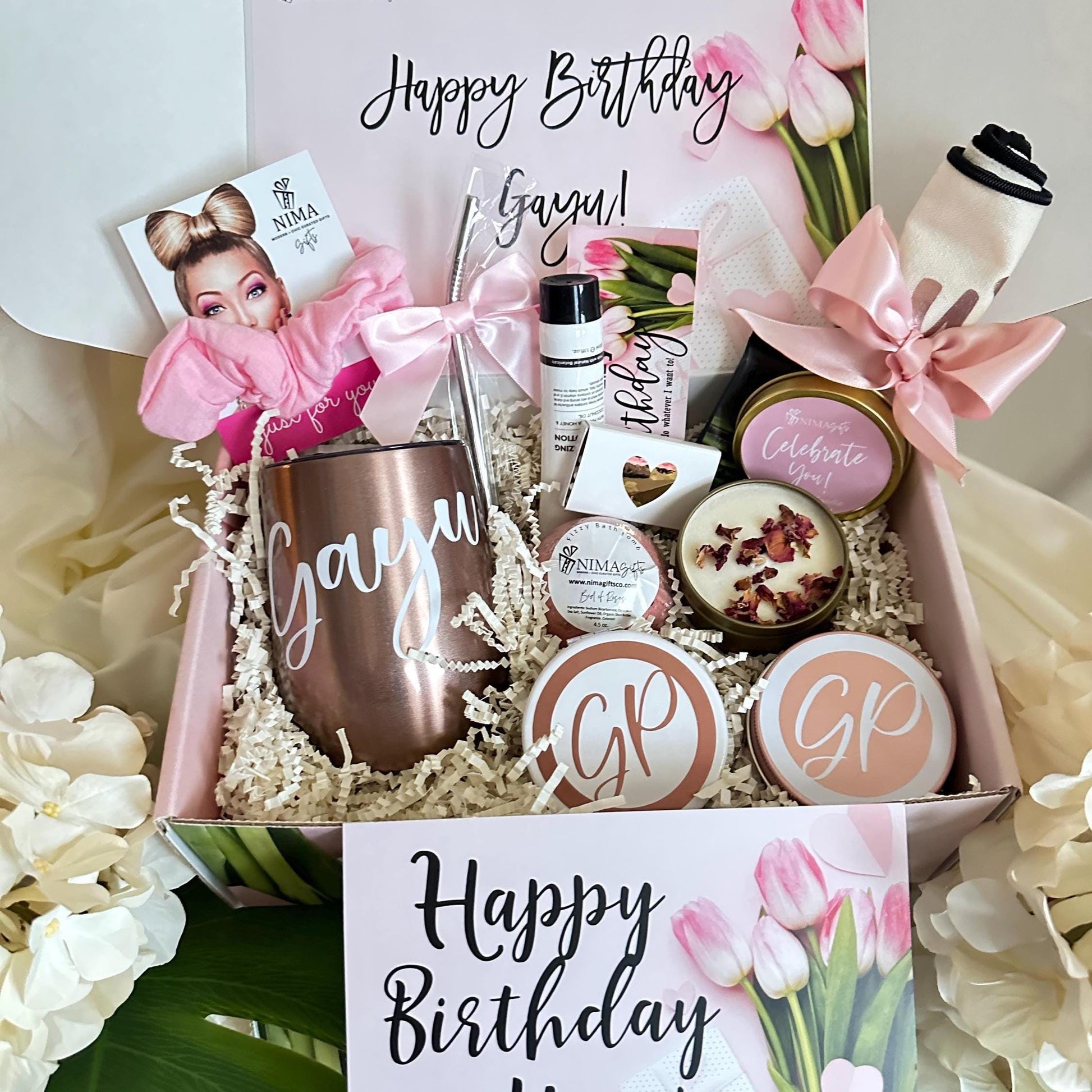 Includes a  pink and white with printed tulips gift box filled with various items, including a personalized tumbler, bath bomb, candles, and a hair scrunchie. The box also includes a card that says "Happy Birthday".
