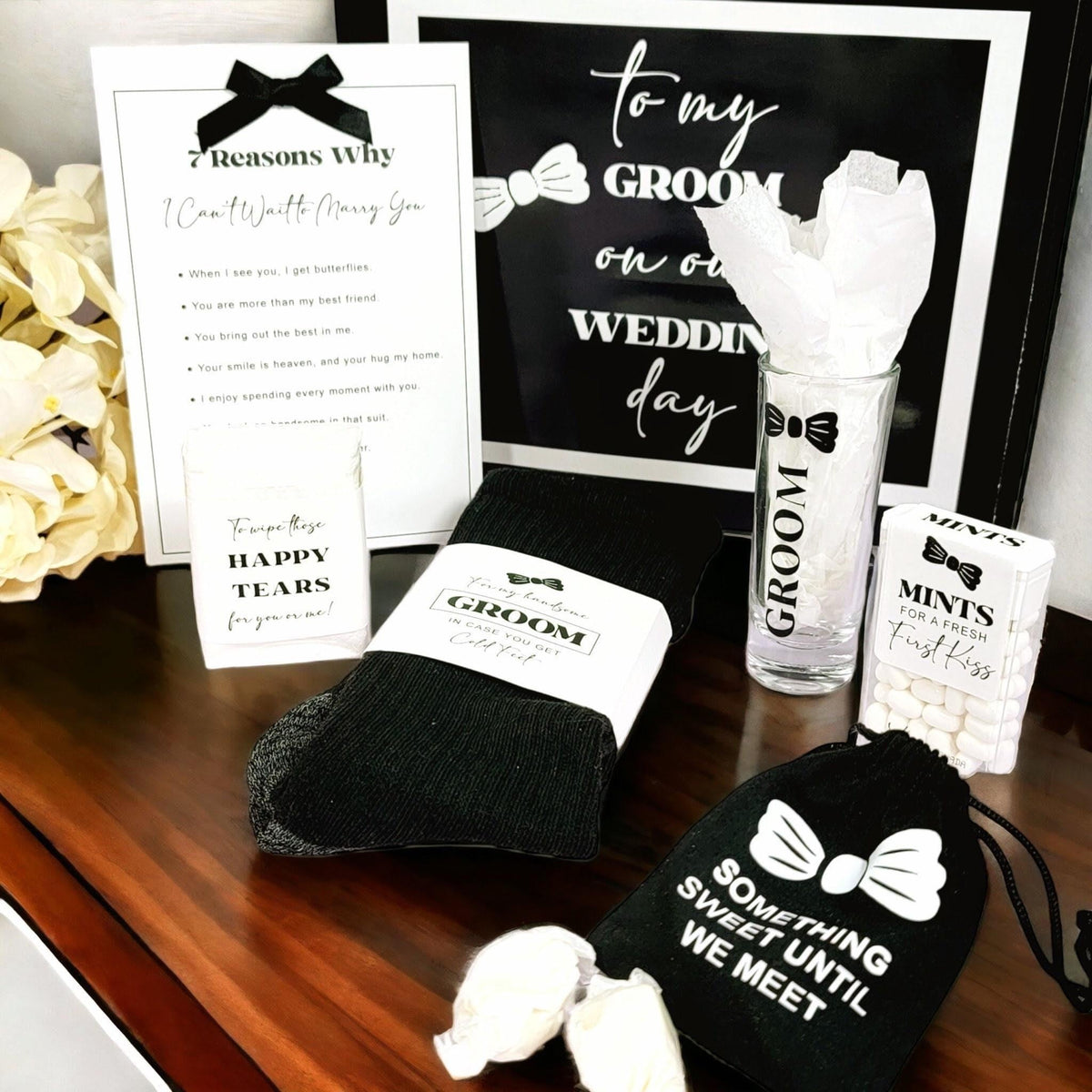 This bride to groom day of wedding gift box is not just a gift box; it's an experience that sets the tone for your unforgettable day. Make your groom's heart melt with this thoughtful, stylish, and unique gift box that contains a pair socks that have grooms initials on them, a shot glass that says groom, a box of mints for a fresh first kiss, a pack of tissues to wipe away those tears, and a black velure bag that says “Something Sweet Until we Meet” or “Groom’s Courage” on it filled with