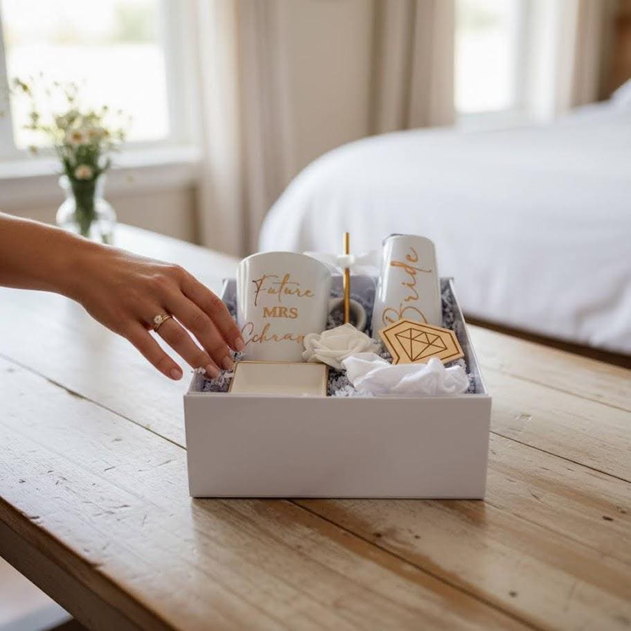 This Personalized Bride to Be Engagement Gift Box is filled with a  personalized coffee mug, personalized bride champagne tumbler with a gold metal straw and personalized satin bow, personalized ring dish, a white satin hair scrunchie and a white foam rose. A greeting card to make your wishes and ask packed in a white magnetic keepsake gift box personalized just for her.