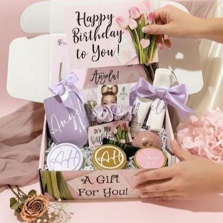 Spa birthday gift box for women that includes a personalized coffee mug, initialed leatherette compact mirror and an initialed candy jar, a bath hand made bath bomb, body lotion, body butter, a hand poured lavender candle and matches, a cotton hair scrunchie, a sachet with lavender leaves and a travel size bar of black soap. Packaged in a beautiful personalized tulip gift box.