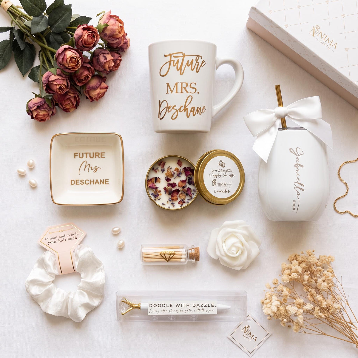 have left of items that are included in the box which include a 15 ounce porcelain white mug with gold personalized letters on top of it. That’s a future Mrs. last name an additional porcelain ring dish with gold trim, and inside it says future Mrs. last name, A hint, poor, lavender candle, a white wine Tumblr engrave with a bright to be first name a gold straw, and a white satin bow, a satin scrunchie, white pen with a large diamond and gold trim, and a bottle of matches with a gold heart.