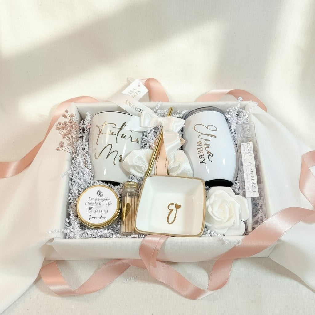 NIMA Gifts white personalized bride-to-be gift box with a mug, wine tumbler, ring dish, candle, pen, matches, scrunchie, and rose accent.