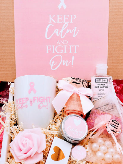 A cancer care gift box for women containing various items such as a white ceramic tea cup, bath crystals, soy candle, and lip balm, personalized with a name and a fighting message.